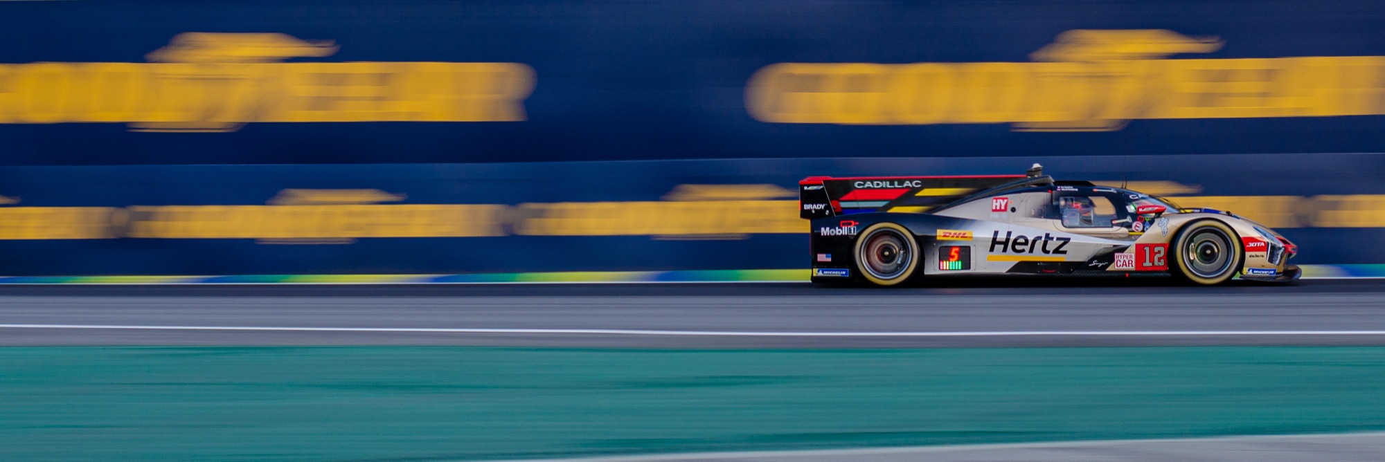 Cadillac V-Series.R #12 da Hertz em velocidade, com os painéis Goodyear varridos ao fundo