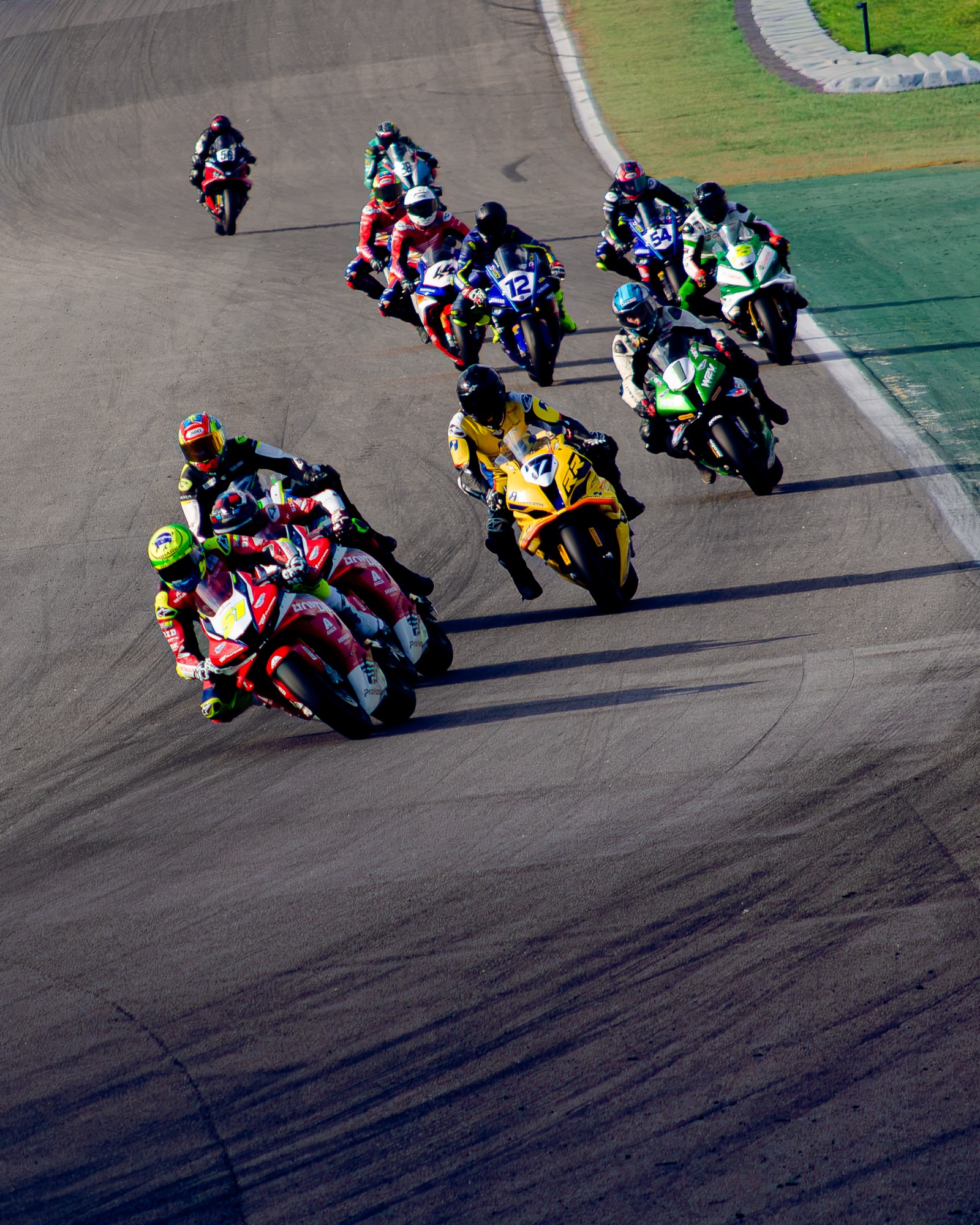 Pelotão de superbikes mergulhando na curva sob luz baixa, a Honda #51 na frente
