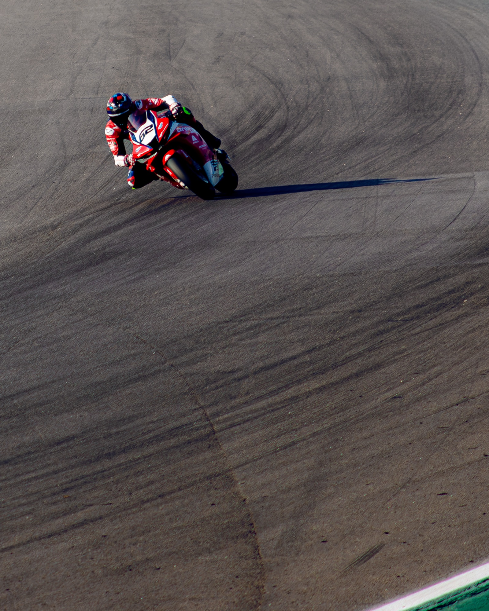 Honda #62 vermelha inclinada na curva, sombra longa sobre o asfalto marcado