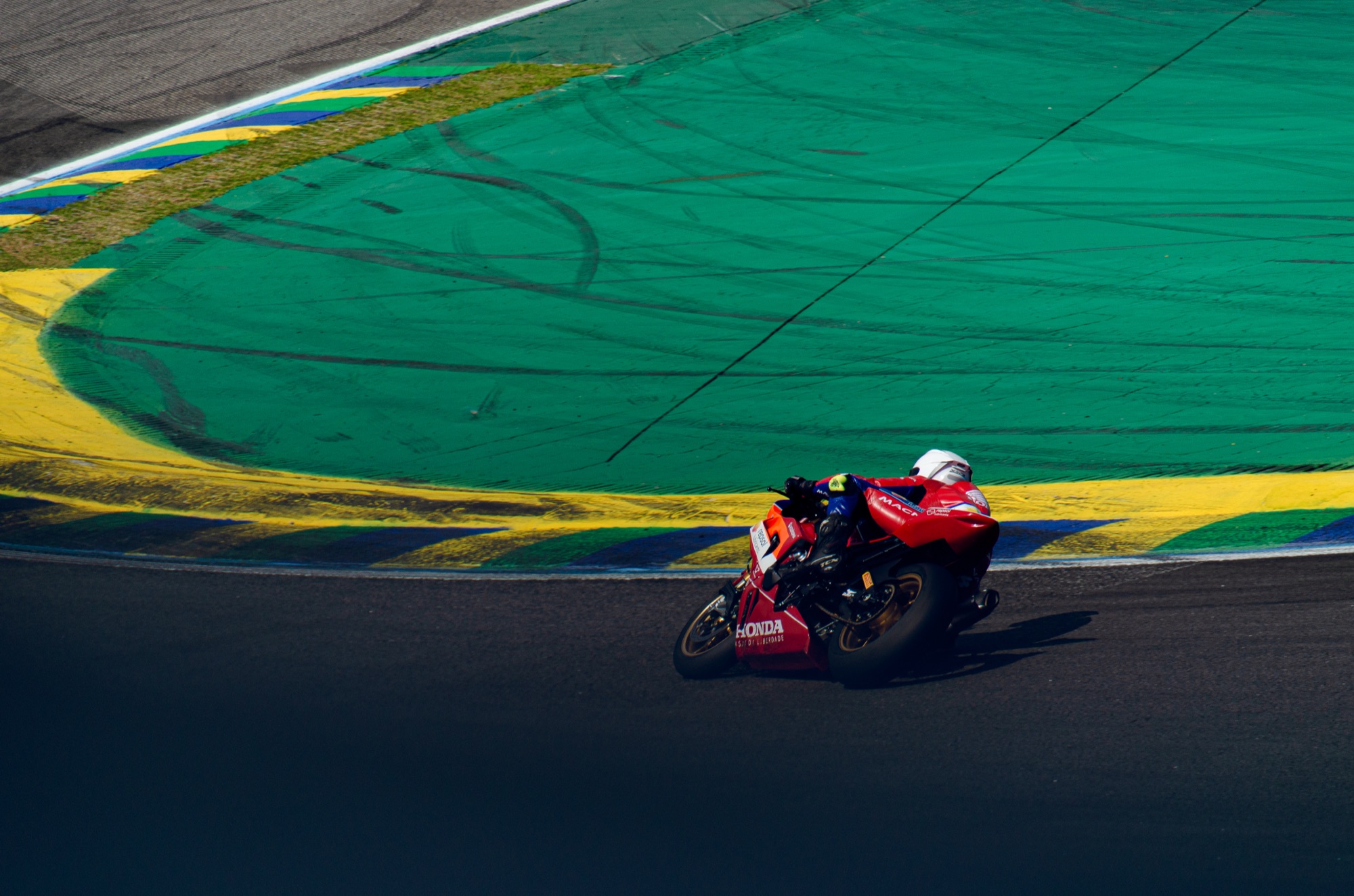 Honda vermelha inclinada rente às zebras verde, amarela e azul de Interlagos
