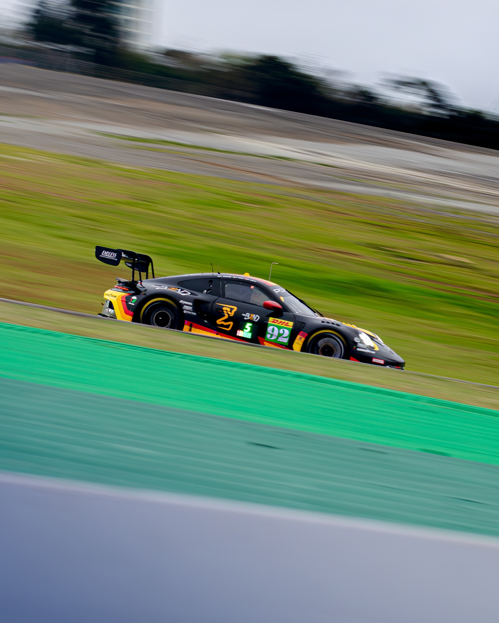 Porsche 911 GT3 R preto e laranja, número 92, em velocidade — fundo varrido pelo panning