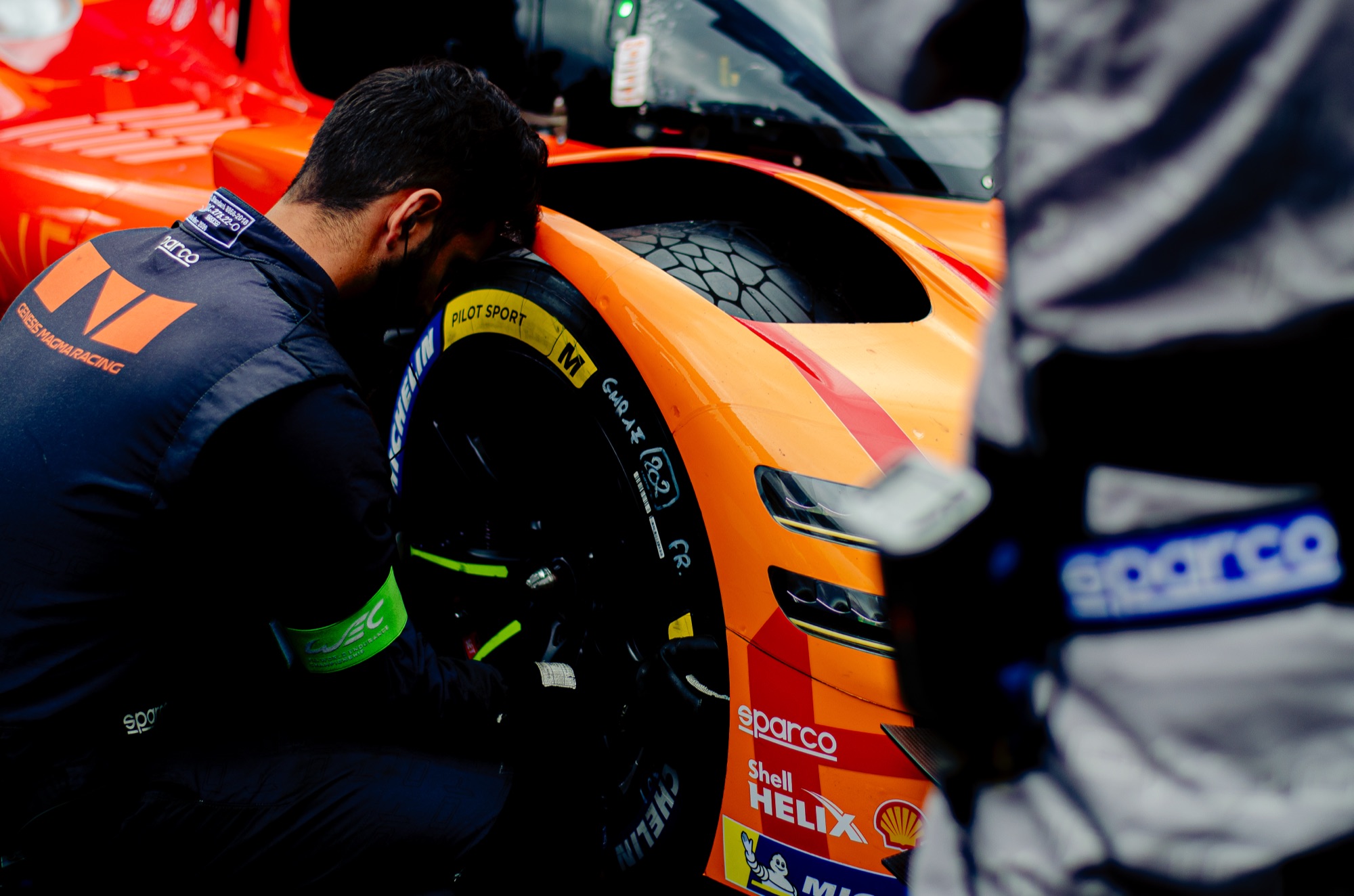 Mecânico da Genesis Magma Racing agachado na roda dianteira do Hypercar laranja