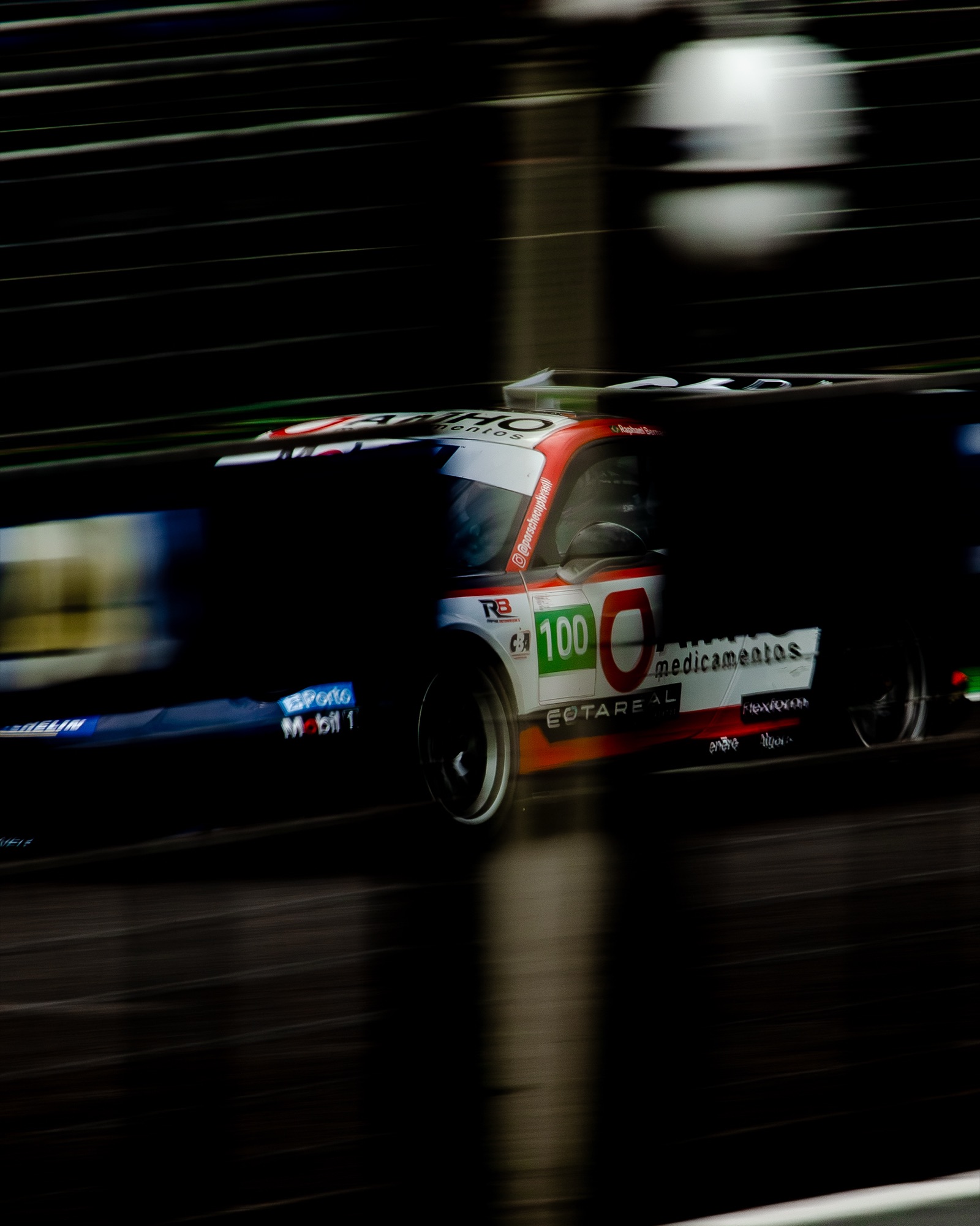 Porsche Cup #100 varrendo o muro dos boxes à noite, tudo desfocado pela velocidade